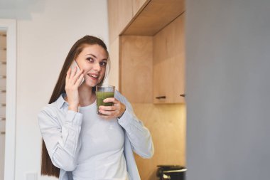 Ev hanımı mutfakta cep telefonuyla konuşuyor.
