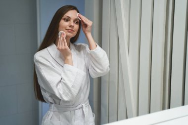 Kadın aynanın önünde makyajını temizliyor.