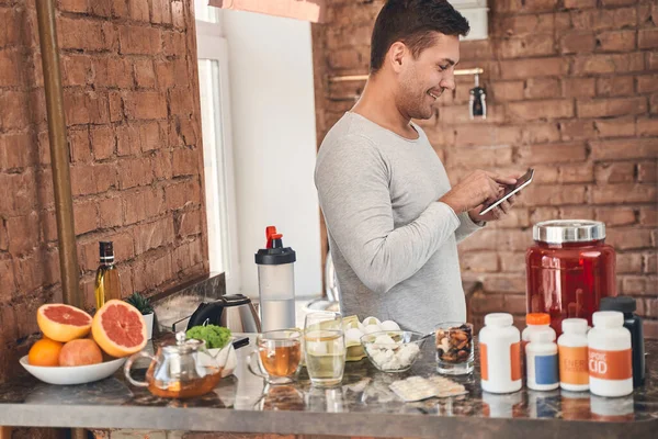 Male with a gadget standing in the kitchen — Stock Photo, Image