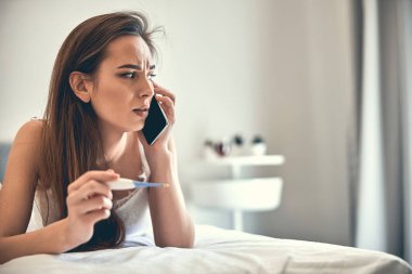 Beyaz, korkmuş kadın evde termometreyle ateşini ölçüyor.