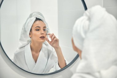Güzel genç bir kadın banyoda kirpik olarak kıvırcık kullanıyor.