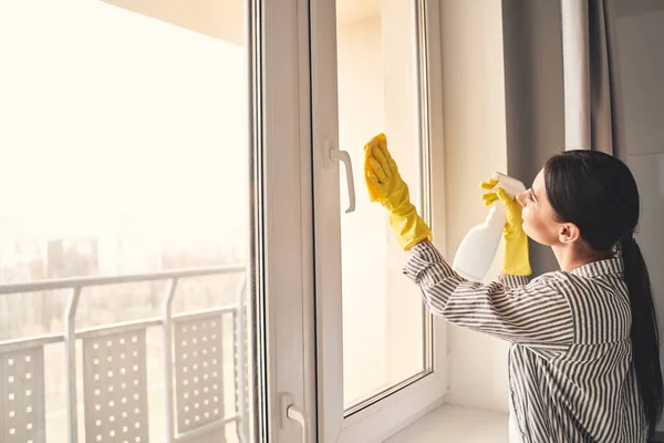 Mujer joven y atenta limpiando ventanas en su piso —  Fotos de Stock