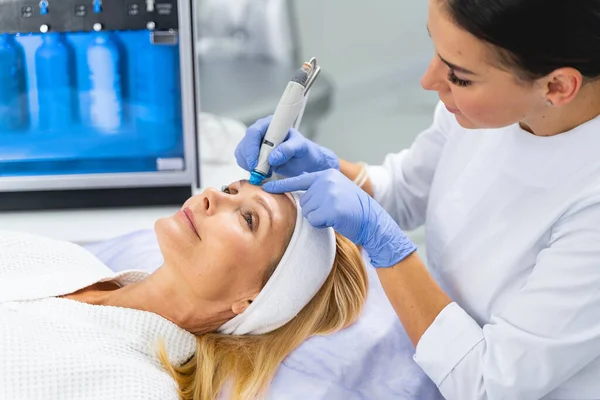 Professional female cosmetologist performing a microdermabrasion treatment — Stock Photo, Image