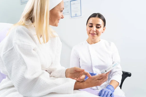 Dermatóloga mirando un producto cosmético en la mano de sus pacientes —  Fotos de Stock