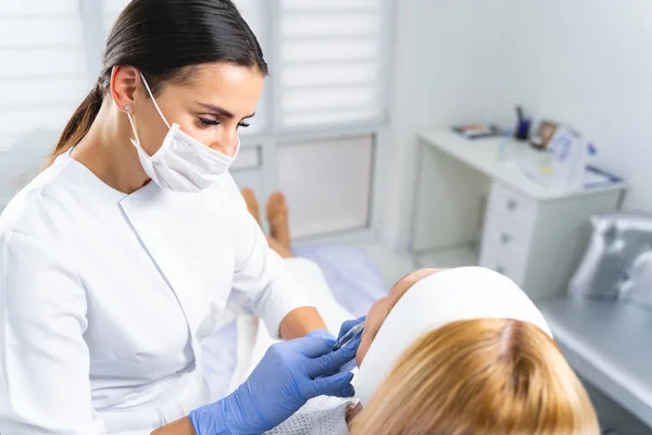 Dermatólogo en una mascarilla que trata a una mujer — Foto de Stock