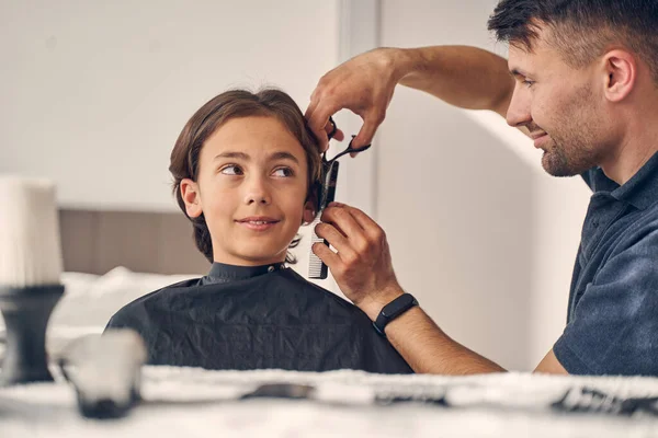 Menino pequeno olhando para o homem cortando seu cabelo — Fotografia de Stock