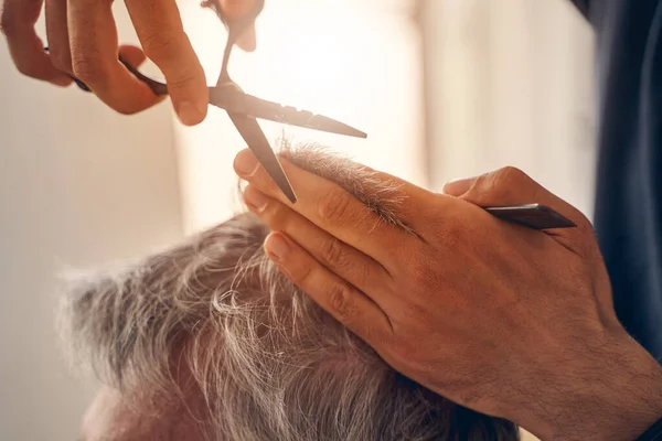 Перукар розрізає волосся людини за допомогою ножиць — стокове фото