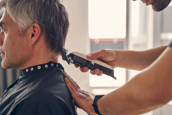 Мужчина стрижет волосы своего взрослого клиента — стоковое фото