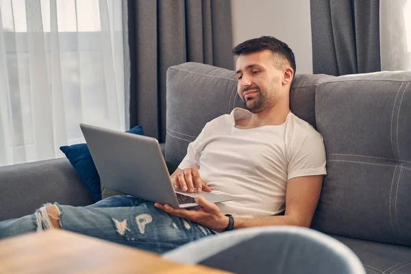 Ung attraktiv leende man sitter på soffan — Stockfoto