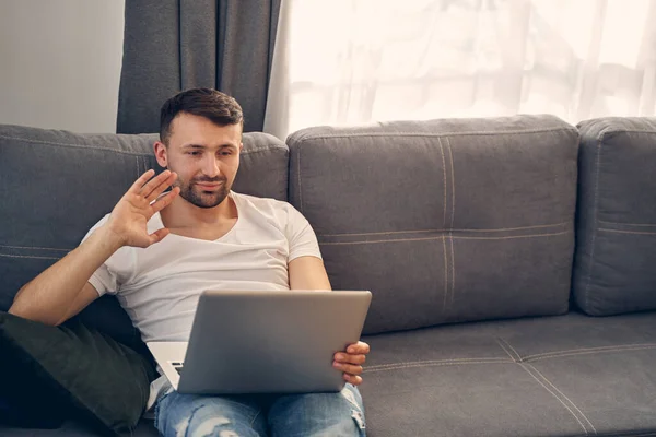 Caucasian young man lying on the sofa using gadgets — Stock Photo, Image