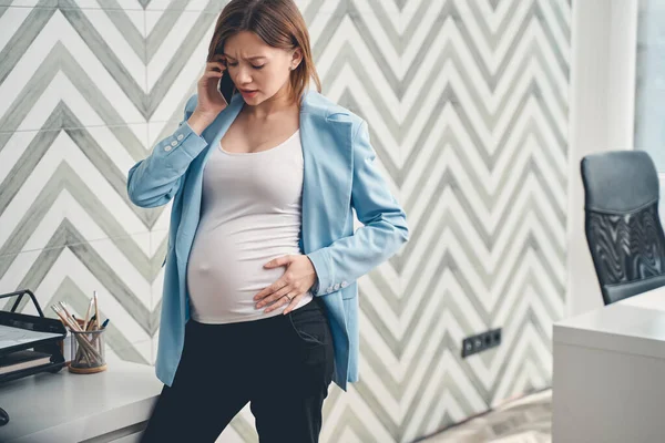 Upprörd gravid kvinna talar på mobiltelefon på kontoret — Stockfoto