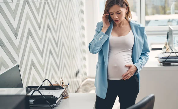 Ofiste cep telefonuyla konuşan rahatsız hamile bir kadın. — Stok fotoğraf