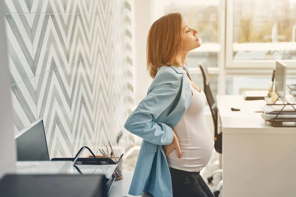 Charmig gravid dam försöker lugna ryggvärk på jobbet — Stockfoto