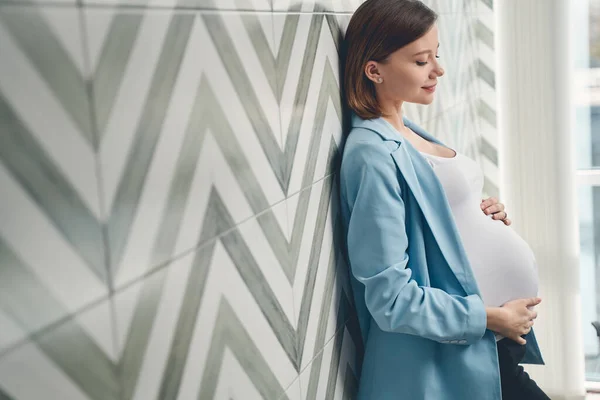 Elbűvölő terhes nő áll a fal mellett. — Stock Fotó