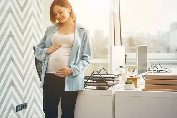 Glädjande gravid kvinna står nära skrivbordet på kontoret — Stockfoto