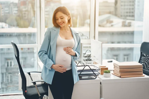 Charming pregnant woman touching her belly and smiling — Stock Photo, Image