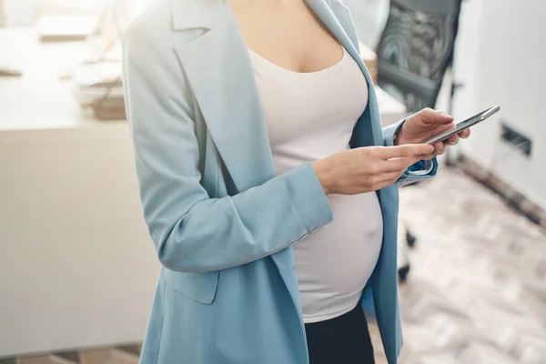 Ung gravid kvinna som använder mobiltelefon på jobbet — Stockfoto