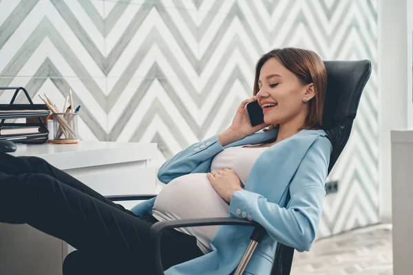 Senhora grávida alegre falando no telefone celular no trabalho — Fotografia de Stock