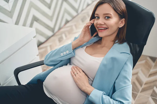 Glädjande gravid dam talar på mobiltelefon på jobbet — Stockfoto