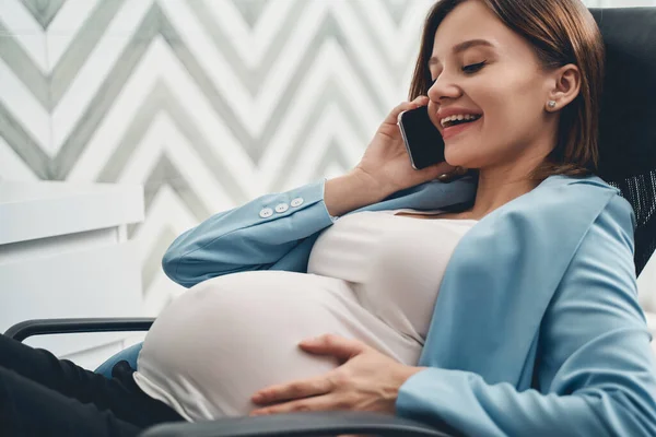 Cheerful pregnant woman having phone conversation at work — Stock Photo, Image