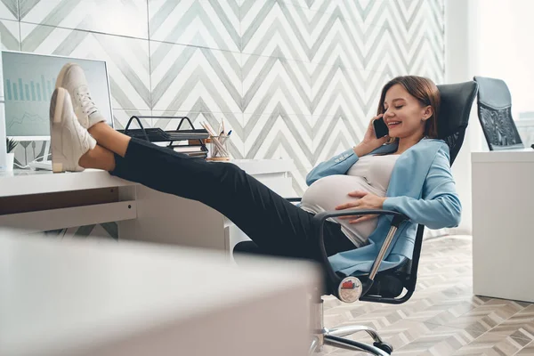 Glad gravid kvinna pratar i mobiltelefon på jobbet — Stockfoto