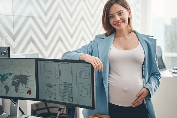 Hermosa mujer embarazada de pie junto a las computadoras en el trabajo — Foto de Stock