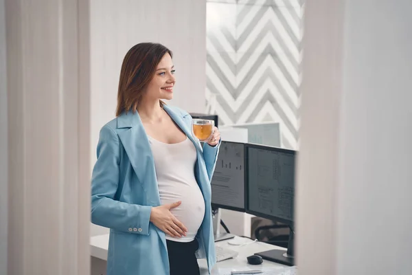 Glad gravid kvinna dricker te på jobbet — Stockfoto