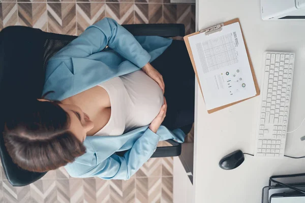 Pregnant woman touching belly while working in office — Stock Photo, Image