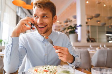 Neşeli genç adam kafede telefon görüşmesi yapıyor.
