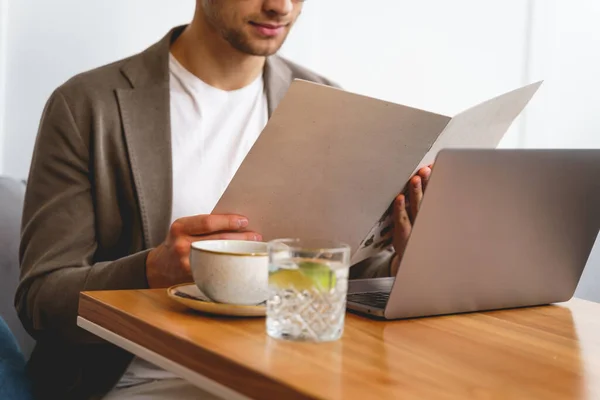 Young man sitting at the table with laptop and reading menu — Stock Photo, Image