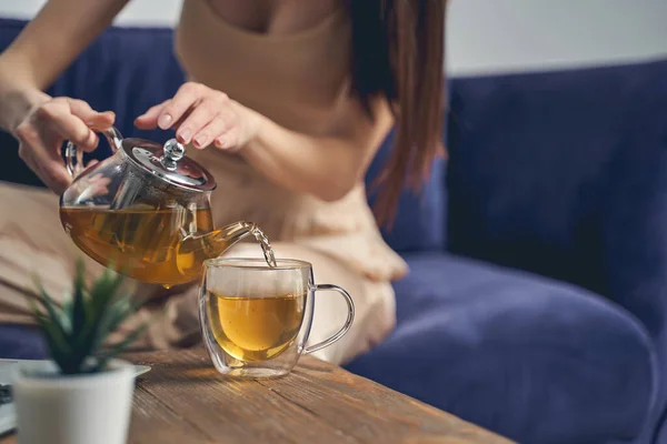 Mujer joven vertiendo té de hierbas en la taza de vidrio — Foto de Stock