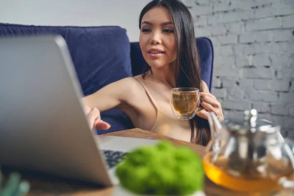 Улыбающаяся молодая женщина пьет чай и пользуется блокнотом — стоковое фото
