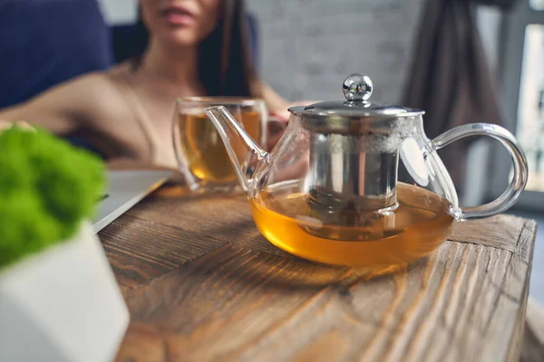 Jonge vrouw zit aan tafel met glazen theepot — Stockfoto