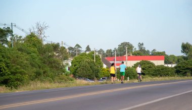 Federal otoyolun kenarında spor yapan insanlar. Bir adam ve bir kadın koşuya hazırlanıyor ve bir erkek de bisiklete biniyor. Hafta sonu spor aktiviteleri.