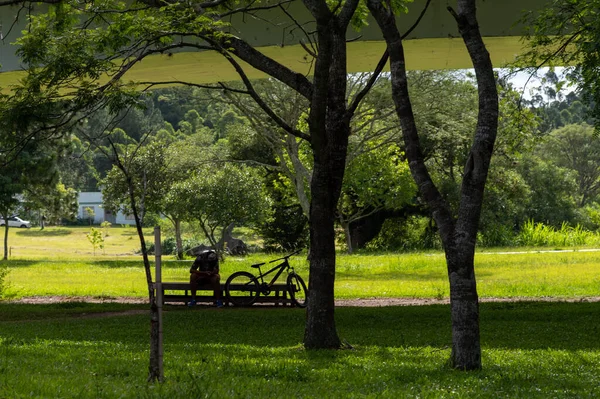 Jovem Sentado Sombra Parque Brincar Com Telemóvel Seu Lado Bicicleta — Fotografia de Stock