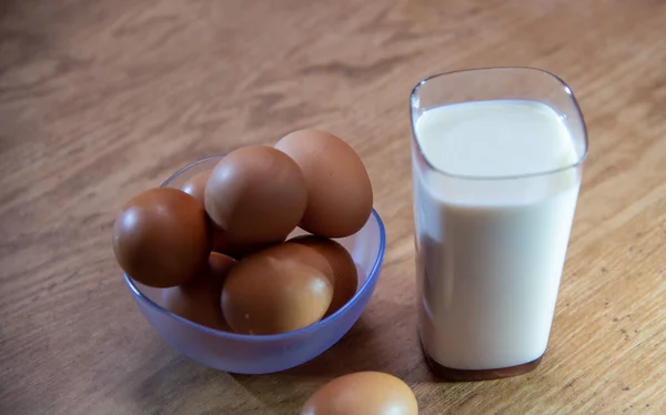 A glass of pure milk and a container with eggs on a wooden table. Human food. Breakfast ingredients. Healthy eating.