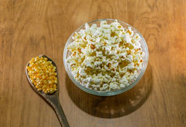 Patlamış mısır taneleri. İçinde mısır tohumu olan tahta bir kaşık. Patlamış mısırlı bir kase patlamış ve tüketime hazır.