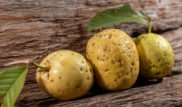 Yellowish pink guava fruits isolated on wooden background. Fresh guavas with green leaves harvested for consumption. Tropical fruits from Brazil. Wood texture. guava leaves and fruits.