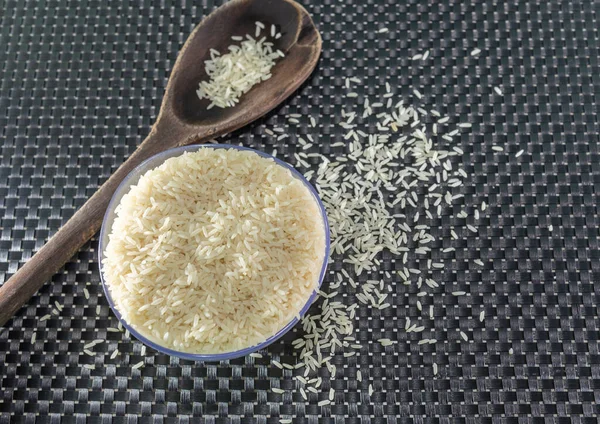 Peeled and processed grain rice on a dark background. Rice cereal and cooking ornaments. Semi-processed grains in a plastic pot and wooden spoons. Foods. Brazilian cuisine.