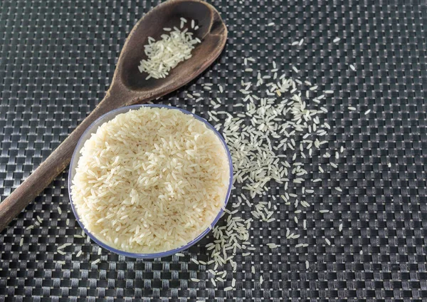 Peeled and processed grain rice on a dark background. Rice cereal and cooking ornaments. Semi-processed grains in a plastic pot and wooden spoons. Foods. Brazilian cuisine.