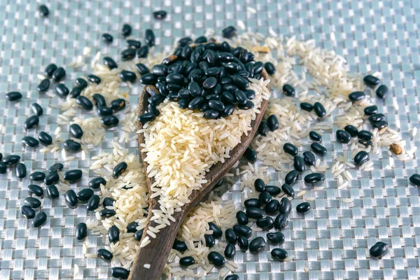 Grains of rice and beans in natura. Mixed grains arranged on a wooden spoon. Cereals for human consumption.