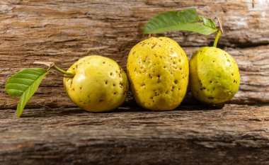 Tahta arka planda izole edilmiş sarımsı pembe guava meyveleri. Tüketim için toplanmış yeşil yapraklı taze guavalar. Brezilya 'dan tropik meyveler. Ahşap dokular. guava yaprakları ve meyveler.