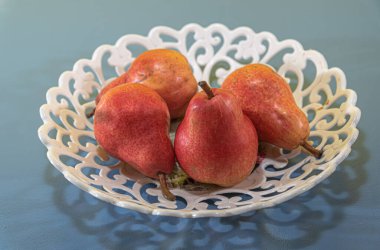 Pyrus comunis l, kırmızı meyveler. Mavi arka planda taze meyve ve beyaz tepsi. Doğal yiyecekler. Armutun yenilebilir meyvesi, Pyrus cinsinden bir ağaç, ılıman bölgelerin en önemli meyvelerinden biri..