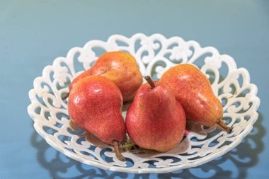 Pyrus comunis l, kırmızı meyveler. Mavi arka planda taze meyve ve beyaz tepsi. Doğal yiyecekler. Armutun yenilebilir meyvesi, Pyrus cinsinden bir ağaç, ılıman bölgelerin en önemli meyvelerinden biri..