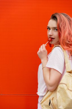 Renkli turuncu duvara karşı kırmızı uçan hailer ve lolipopla güzel gülümseyen hippi kadının moda portresi.