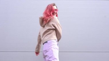 Gri duvarda duran pembe renkli saçları ve neon gözlüklü güzel bir kadın. Şehre. Uçan saç stili. Kentsel