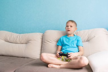 Mavi tişörtlü küçük şirin çocuk elektronik oyunda joystick ile oynuyor.