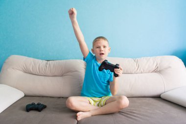 Mavi tişörtlü küçük şirin çocuk elektronik oyunda joystick ile oynuyor.