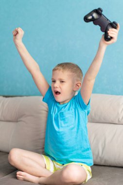 Mavi tişörtlü küçük şirin çocuk elektronik oyunda joystick ile oynuyor.