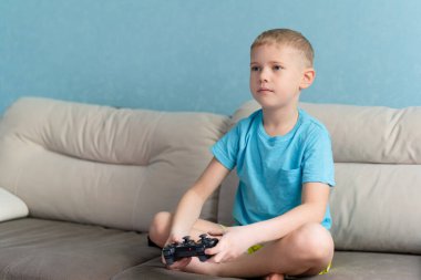 Mavi tişörtlü küçük şirin çocuk elektronik oyunda joystick ile oynuyor.